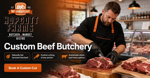 Butcher in black apron cutting custom beef cuts at Hoptcott Farms butcher shop with raw meat displayed on wooden surface